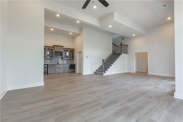 unfurnished living room with ceiling fan, beverage cooler, a high ceiling, and hardwood / wood-style floors