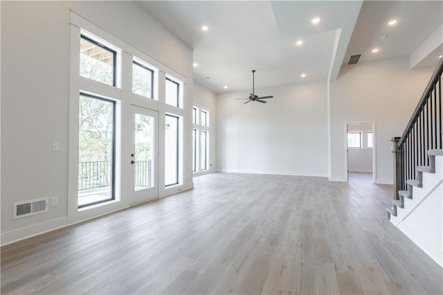 unfurnished living room with a high ceiling, ceiling fan, a healthy amount of sunlight, and light hardwood / wood-style flooring