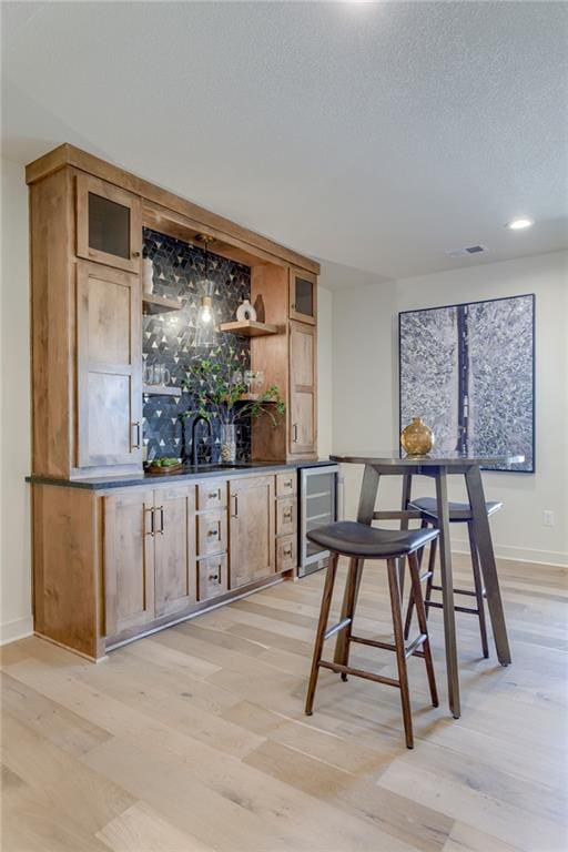 bar with wine cooler, a textured ceiling, sink, and light hardwood / wood-style flooring