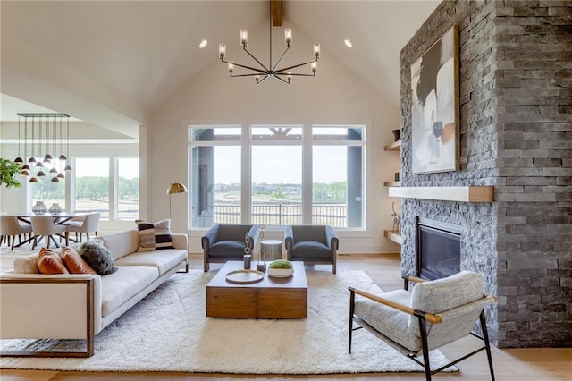 living room with plenty of natural light, a stone fireplace, a chandelier, and light wood-type flooring