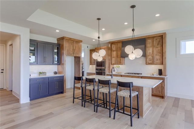 kitchen with pendant lighting, a center island with sink, stainless steel appliances, and light wood-type flooring