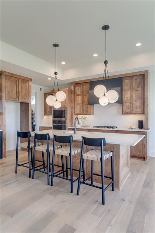 kitchen featuring decorative light fixtures, a kitchen bar, light hardwood / wood-style flooring, stainless steel appliances, and a center island with sink