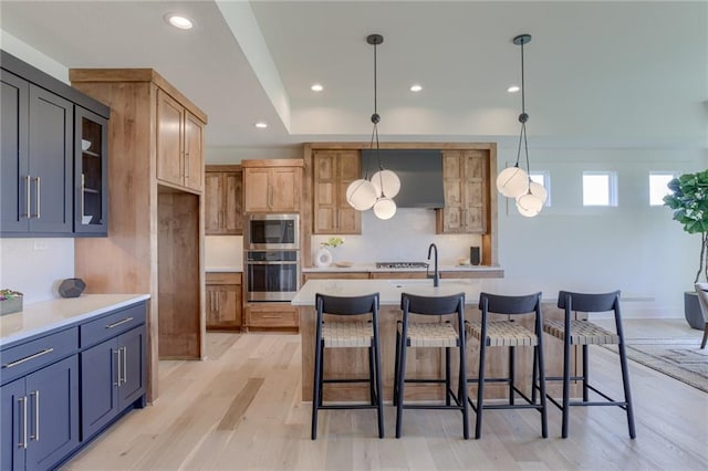 kitchen with an island with sink, hanging light fixtures, light hardwood / wood-style flooring, stainless steel appliances, and a kitchen bar