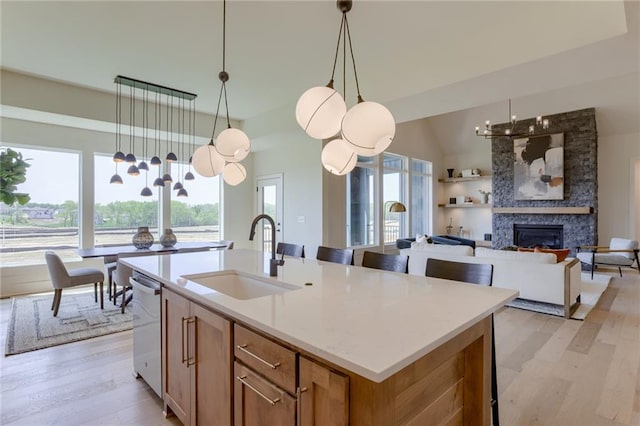 kitchen with hanging light fixtures, a kitchen island with sink, a fireplace, sink, and light hardwood / wood-style flooring