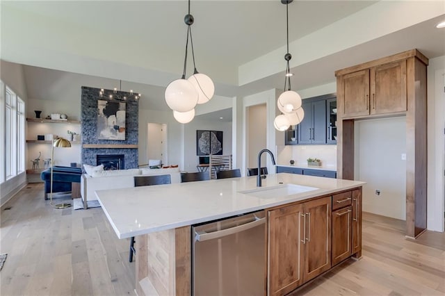 kitchen with pendant lighting, dishwasher, a center island with sink, and a large fireplace