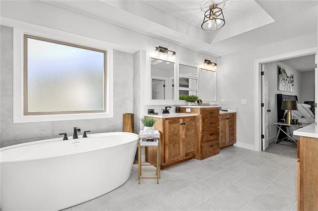 bathroom featuring tile flooring, a chandelier, vanity with extensive cabinet space, a washtub, and a tray ceiling