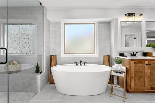 bathroom with tile walls, tile floors, a bath, and vanity with extensive cabinet space