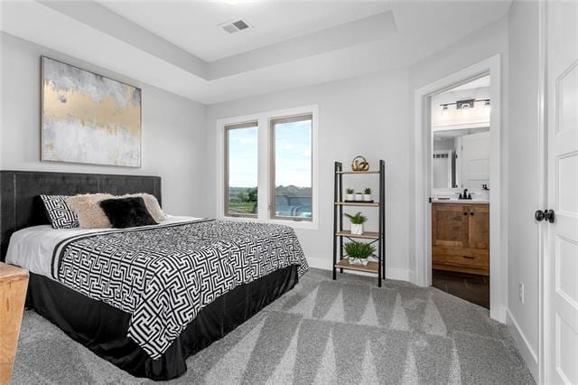 carpeted bedroom featuring connected bathroom and a tray ceiling