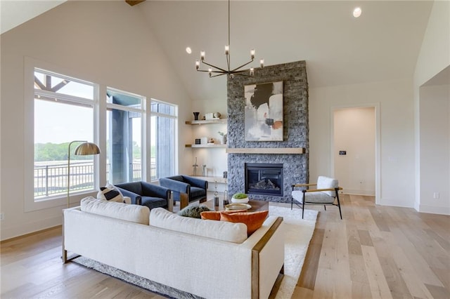 living room with high vaulted ceiling, an inviting chandelier, a fireplace, and light wood-type flooring