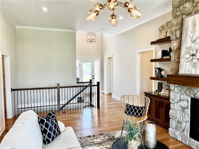 living room with ornamental molding, a notable chandelier, a stone fireplace, and light hardwood / wood-style flooring