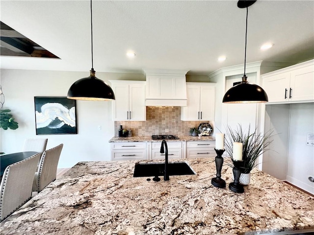 kitchen with decorative light fixtures, white cabinets, backsplash, custom range hood, and light stone counters