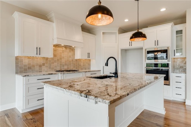 kitchen with hanging light fixtures, an island with sink, tasteful backsplash, and sink