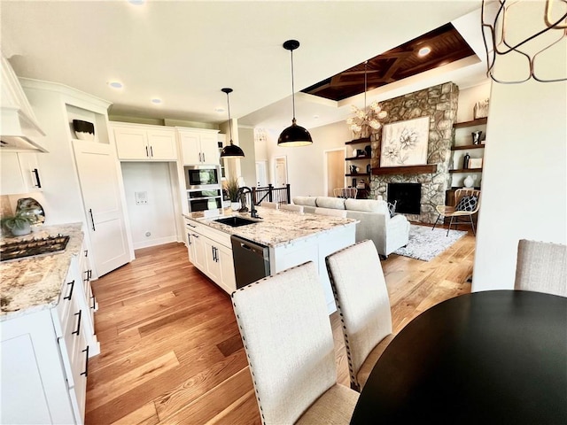 kitchen featuring white cabinets, hanging light fixtures, light wood-type flooring, and a stone fireplace