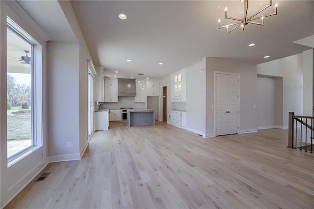 unfurnished living room with light hardwood / wood-style flooring, a healthy amount of sunlight, a notable chandelier, and sink