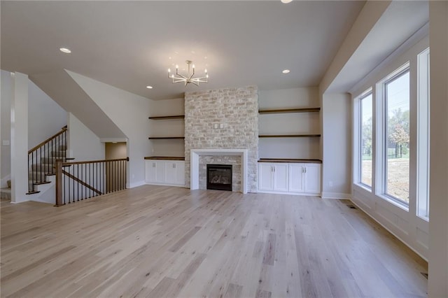 unfurnished living room with a large fireplace, an inviting chandelier, and light hardwood / wood-style flooring