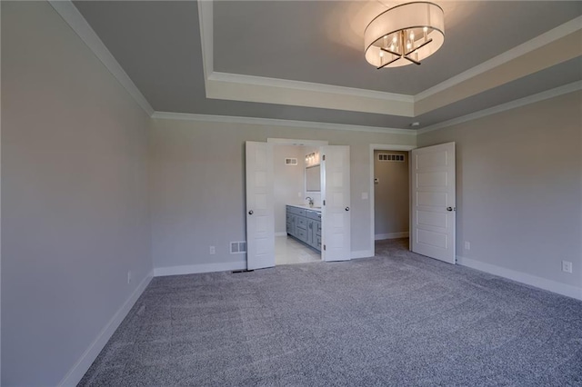 unfurnished bedroom featuring a raised ceiling, ensuite bath, light colored carpet, and ornamental molding