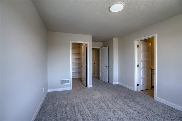 unfurnished bedroom featuring a spacious closet, ensuite bathroom, a textured ceiling, light carpet, and a closet