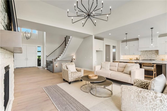 living room with an inviting chandelier, a brick fireplace, a towering ceiling, and light wood-type flooring