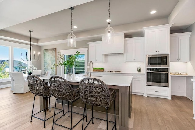 kitchen with a sink, stainless steel appliances, a center island with sink, light wood finished floors, and light countertops