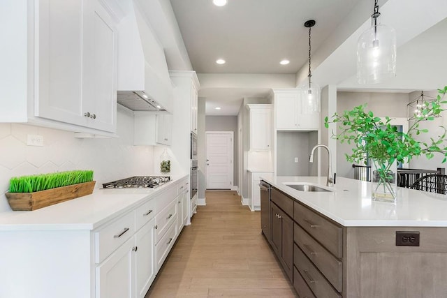 kitchen with a sink, stainless steel appliances, white cabinets, a kitchen island with sink, and light wood-type flooring