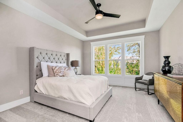 carpeted bedroom with a raised ceiling, baseboards, and a ceiling fan