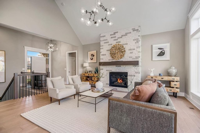 living area featuring wood finished floors, high vaulted ceiling, visible vents, a fireplace, and an inviting chandelier