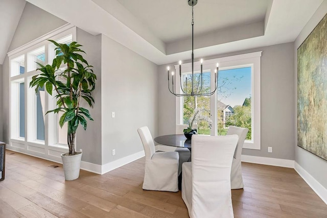 dining room featuring a tray ceiling, an inviting chandelier, wood-type flooring, and baseboards