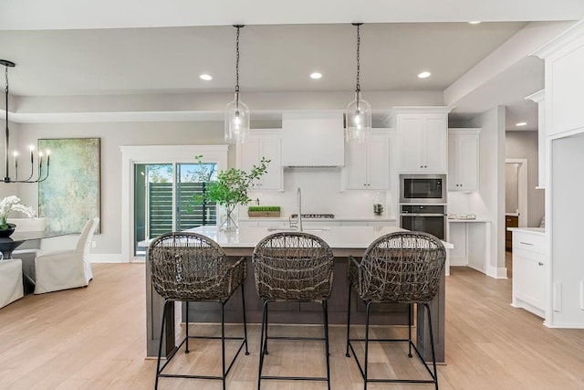 kitchen featuring appliances with stainless steel finishes, a center island with sink, white cabinetry, light countertops, and light wood-style floors