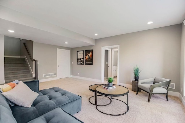 living area featuring light colored carpet, visible vents, baseboards, and stairway