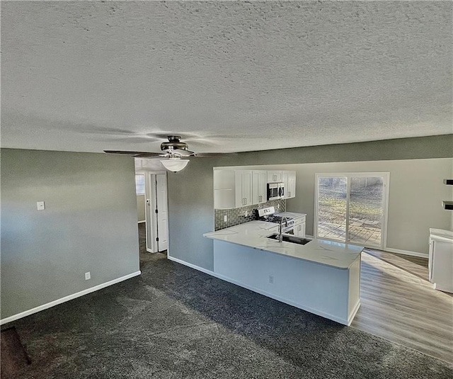 kitchen with dark wood-type flooring, white cabinetry, stainless steel appliances, kitchen peninsula, and ceiling fan