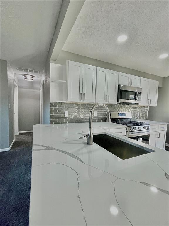 kitchen with white cabinetry, appliances with stainless steel finishes, light stone counters, and dark carpet