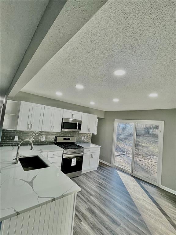 kitchen featuring white cabinetry, light hardwood / wood-style flooring, appliances with stainless steel finishes, and light stone countertops