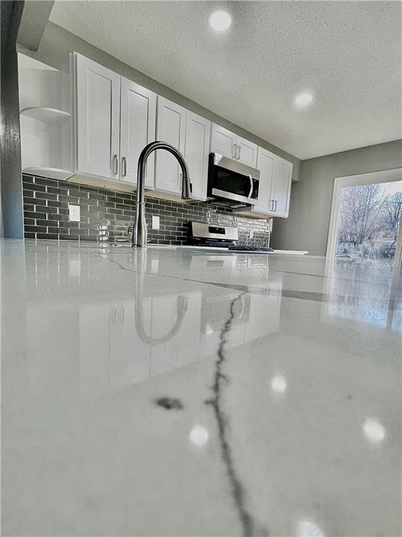 kitchen featuring white cabinets, backsplash, a textured ceiling, and light stone countertops