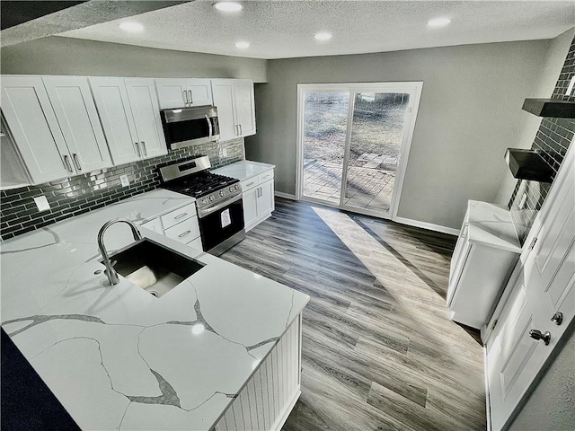 kitchen featuring sink, light hardwood / wood-style floors, stainless steel appliances, light stone countertops, and white cabinetry