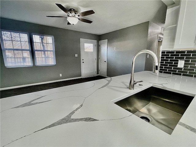 kitchen with ceiling fan, white cabinetry, sink, and light stone counters