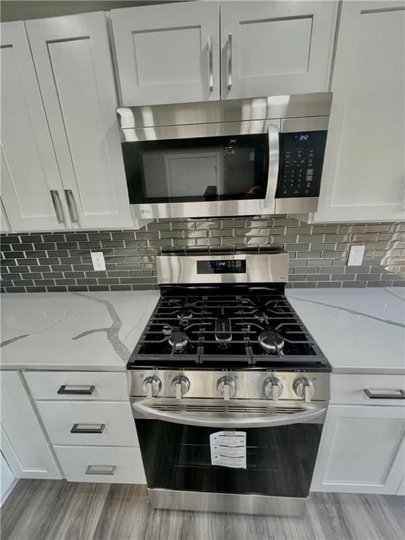 kitchen with light hardwood / wood-style flooring, white cabinetry, appliances with stainless steel finishes, and light stone counters