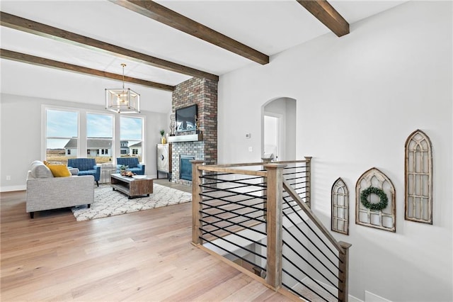 interior space featuring a brick fireplace, brick wall, beamed ceiling, a notable chandelier, and light wood-type flooring