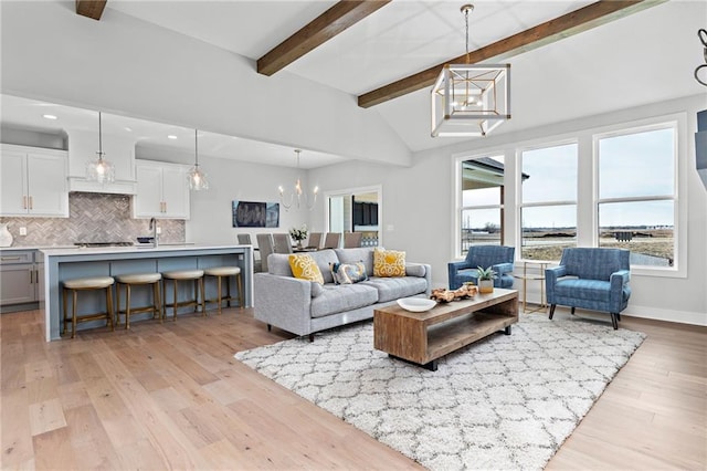 living room featuring light hardwood / wood-style flooring, sink, a notable chandelier, and vaulted ceiling with beams