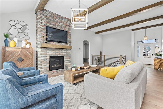 living room featuring a chandelier, wood-type flooring, a brick fireplace, and vaulted ceiling with beams