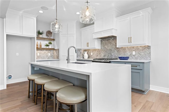 kitchen featuring sink, tasteful backsplash, light wood-type flooring, hanging light fixtures, and a kitchen island with sink