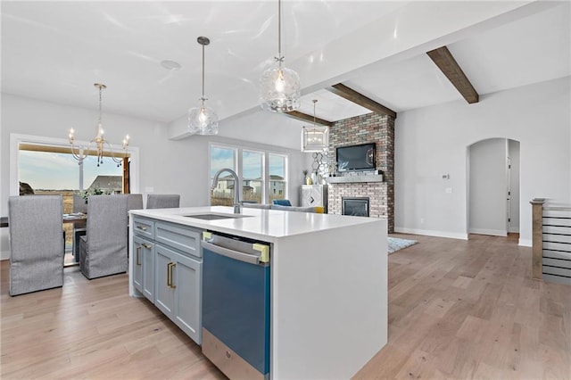 kitchen with a fireplace, sink, stainless steel dishwasher, light hardwood / wood-style flooring, and a kitchen island with sink