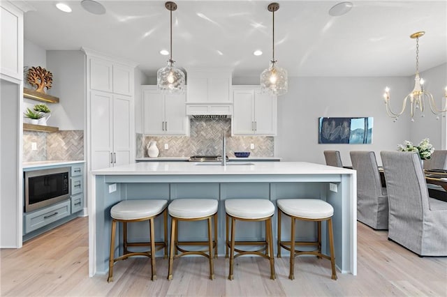 kitchen with backsplash, pendant lighting, light hardwood / wood-style floors, and stainless steel microwave