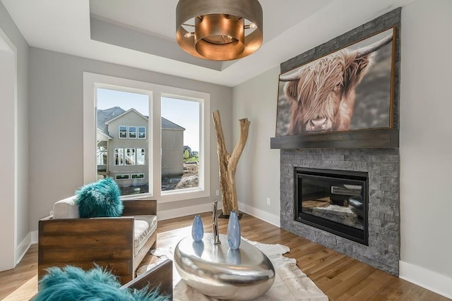 living area with a raised ceiling, light hardwood / wood-style flooring, and a fireplace