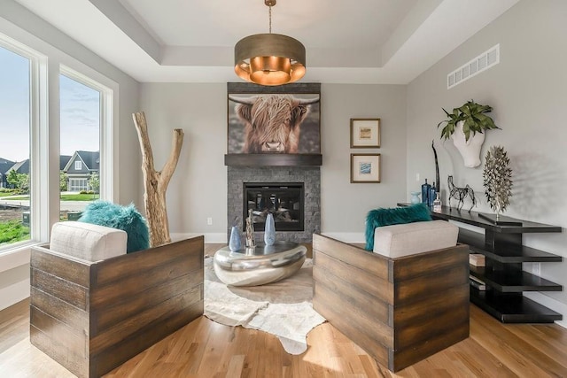 living room featuring a fireplace, light hardwood / wood-style floors, and a raised ceiling