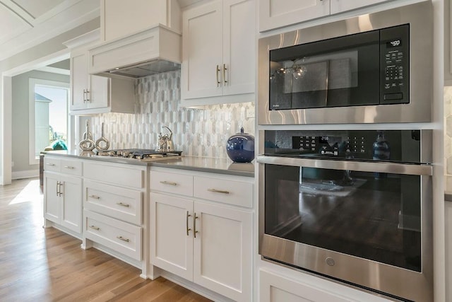 kitchen with white cabinets, light hardwood / wood-style flooring, stainless steel appliances, custom exhaust hood, and tasteful backsplash