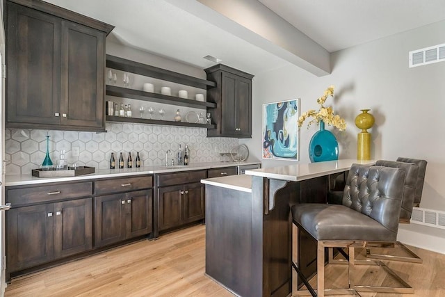 bar featuring backsplash, dark brown cabinets, and light hardwood / wood-style flooring