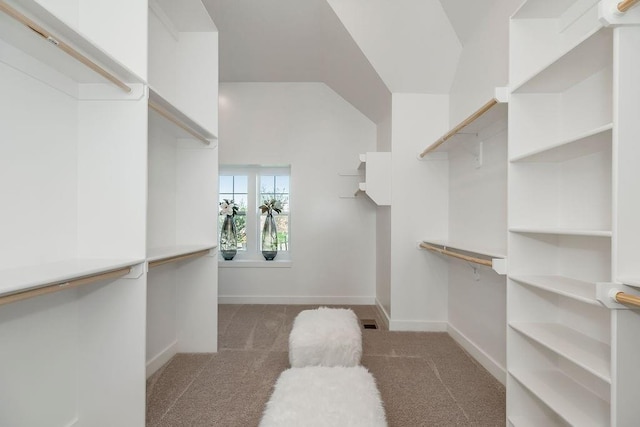 spacious closet featuring vaulted ceiling and dark colored carpet