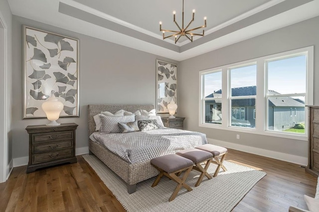 bedroom featuring an inviting chandelier, multiple windows, dark hardwood / wood-style floors, and a raised ceiling