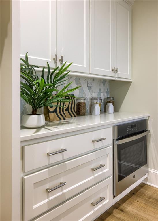 bar with backsplash, wall oven, light wood-type flooring, and white cabinetry