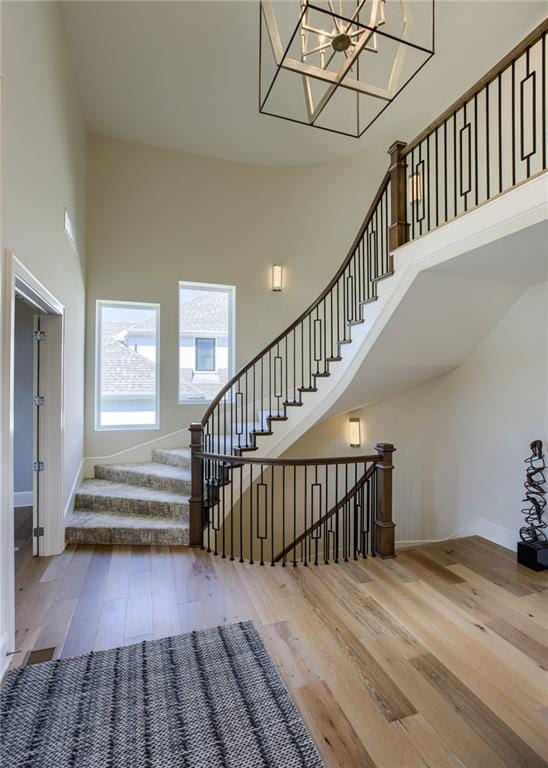 stairway with a high ceiling, a notable chandelier, and light wood-type flooring